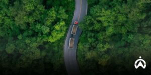 Truk merah Cartrack dengan dua bak muatan melintasi jalan berliku di tengah hutan