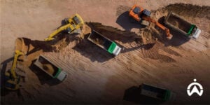 Pemandangan udara alat berat ekskavator memuat tanah ke jajaran truk di lokasi proyek