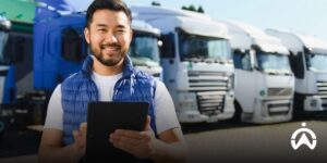 Man wearing blue vest holding tablet in front of fleet of delivery trucks