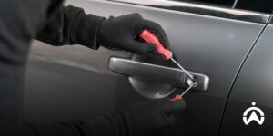Tangan mengenakan sarung tangan sedang membobol pintu mobil dengan obeng sebagai ilustrasi upaya pencurian kendaraan dan meningkatnya kriminalitas.