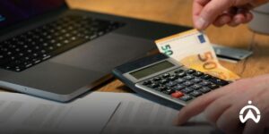 A person manages vehicle operating costs using a calculator and laptop via the Cartrack Fleet Web dashboard.