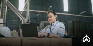 Employees use fleet management software on laptops to improve the efficiency of fleet operations within an industrial warehouse.