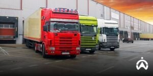 Tiga truk di depan gudang menunjukkan teknologi manajemen armada untuk industri manufaktur.