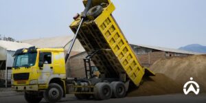 Dump truck kuning sedang menumpahkan pasir di lokasi konstruksi