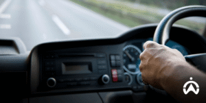Close-up tangan pengemudi pada setir mobil di jalan raya untuk antisipasi situasi darurat di perjalanan dengan teknologi Cartrack.