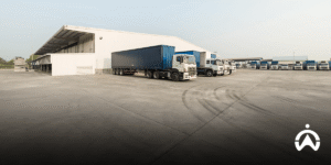 Barisan truk logistik biru putih di area bongkar muat gudang untuk efisiensi visibilitas supply chain end-to-end.