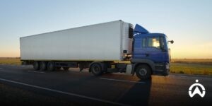 A blue logistics truck with a refrigerated trailer stops at the side of the road at sunset.
