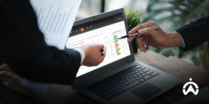 Two professionals are analyzing data on a vehicle tracking device via a laptop to monitor the operational status displayed in a colored graph.