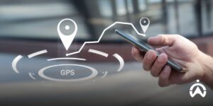 A person holds a smartphone displaying digital navigation icons to monitor the vehicle's GPS tracker and telematics in real-time.