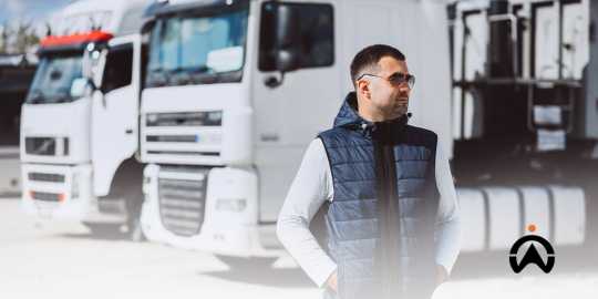Pengemudi berdiri di depan truk, didukung sistem manajemen armada untuk meningkatkan keselamatan berkendara.