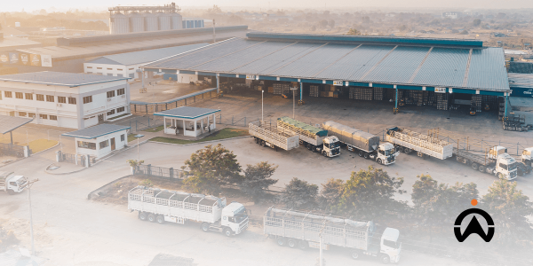 Aerial view dari gudang industri besar dengan armada truk logistik, menggunakan platform manajemen tugas untuk perkembangan bisnis.