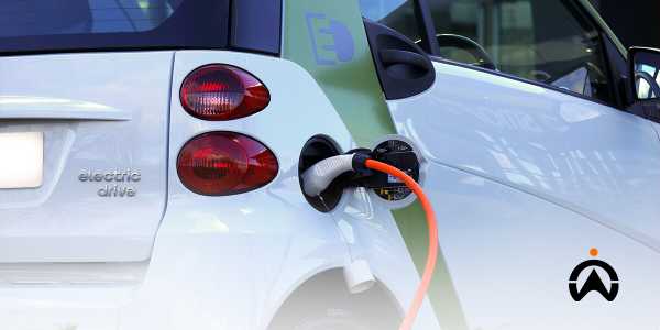 Mobil listrik putih sedang mengisi daya dengan kabel oranye untuk transisi elektrifikasi armada.