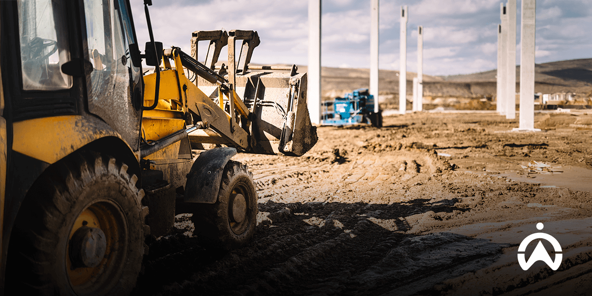 Alat berat backhoe loader di area proyek, menggunakan fleet management system untuk industri pertambangan.
