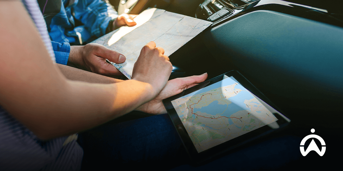 Dua orang di mobil membandingkan peta fisik dengan perangkat lunak optimasi rute di tablet untuk perencanaan armada