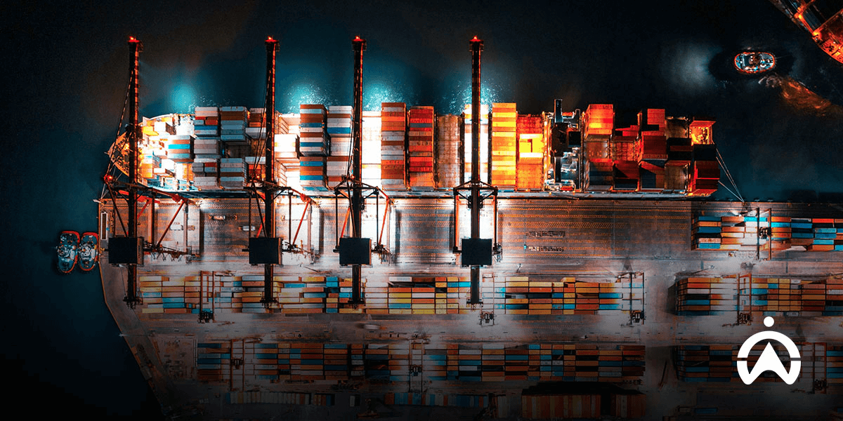 Pemandangan udara malam hari kapal kargo di pelabuhan dengan peti kemas, mengilustrasikan proses manajemen armada dalam logistik modern