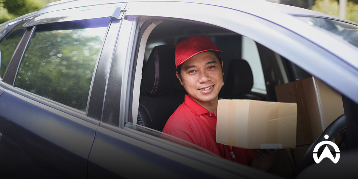Kurir tersenyum memegang paket di dalam mobil sebagai bukti pengiriman (proof of delivery) yang aman.