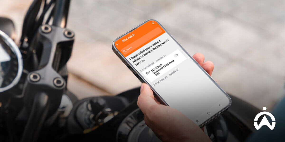 Seseorang memegang smartphone yang menampilkan aplikasi pelacak di dekat stang untuk fungsi GPS tracker anti-maling sepeda motor.