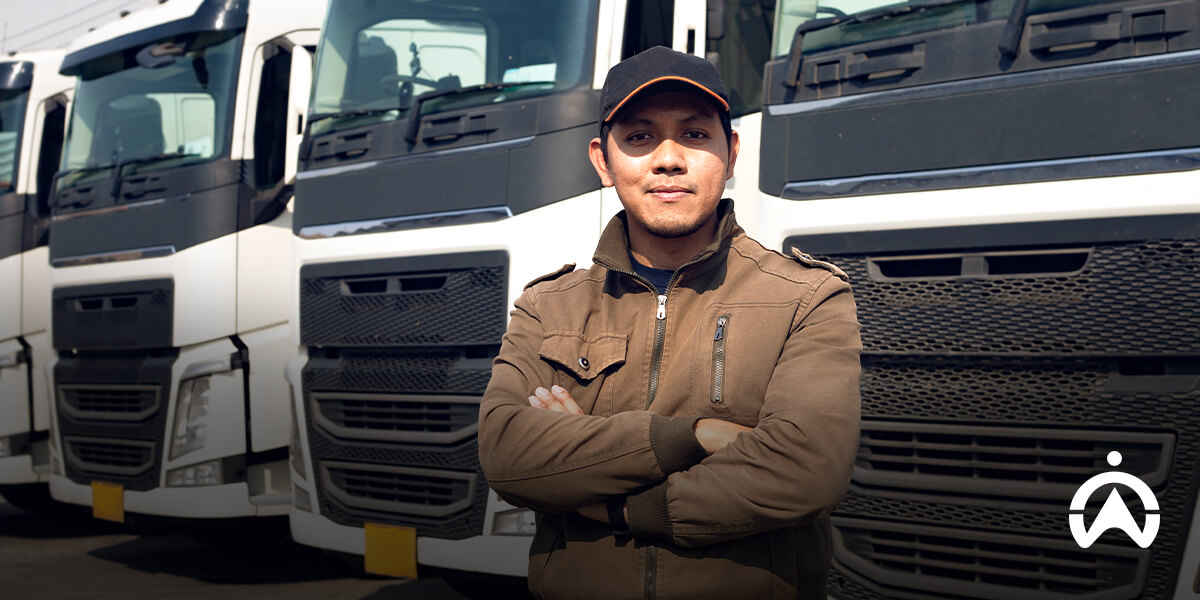 Pria berdiri di depan deretan truk logistik pengguna software manajemen armada perusahaan.