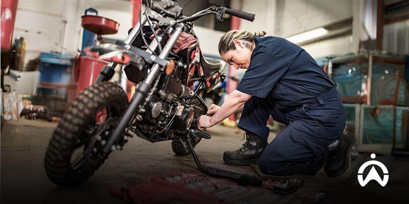Mekanik sedang memperbaiki motor di bengkel, ideal untuk pemasangan GPS tracker motor terbaik.