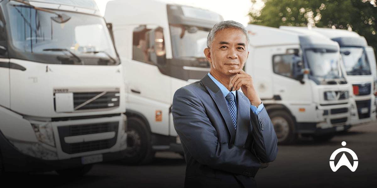 Pengusaha berdiri di depan armada truk untuk mengilustrasikan sistem driver management dan pengelolaan transportasi logistik.