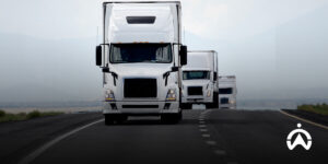 Three white semitrailer trucks pass on the toll road to save fuel efficiently.